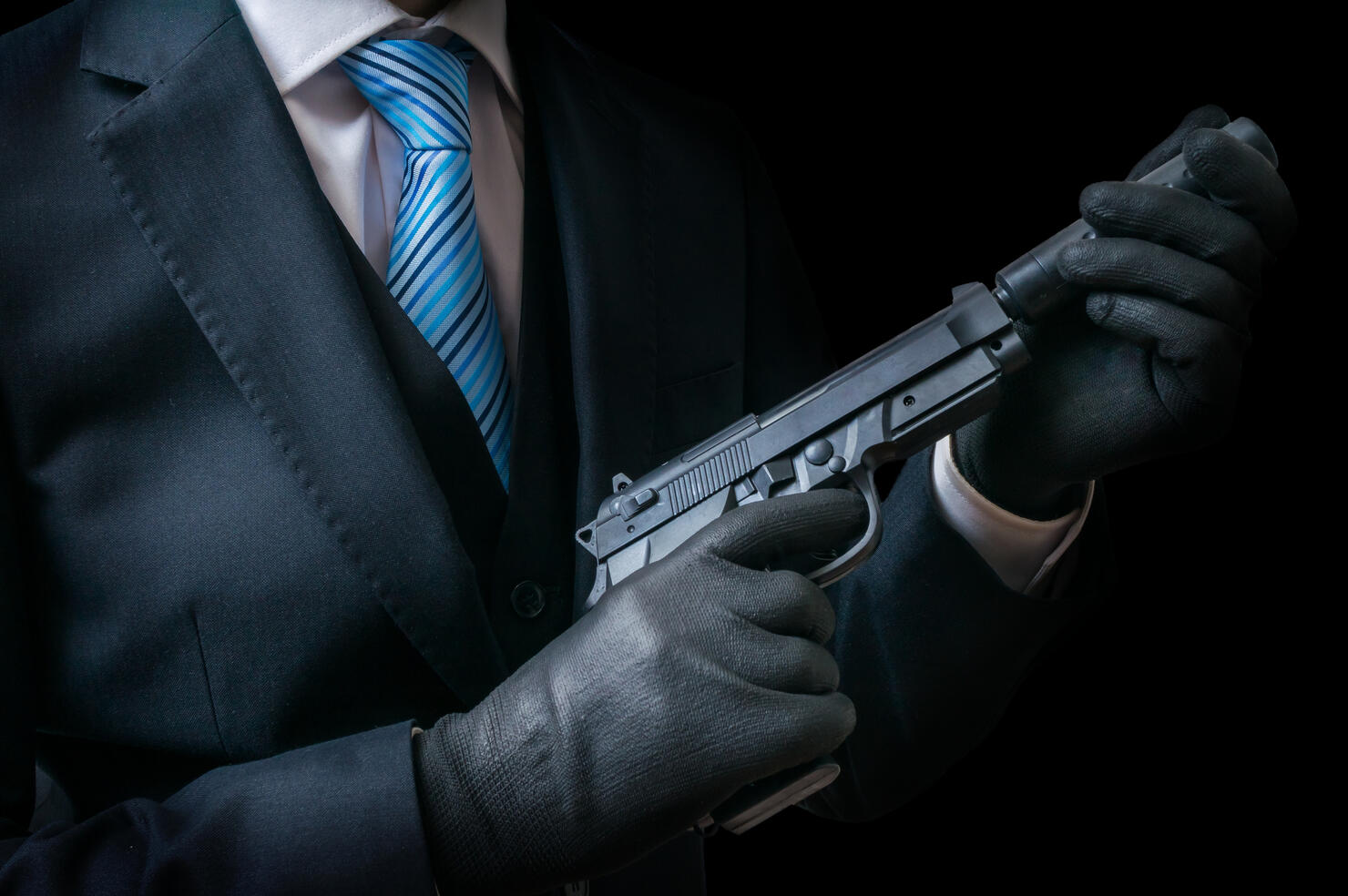 Mafia man holds pistol with silencer in hands. Low key.