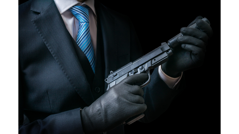 Mafia man holds pistol with silencer in hands. Low key.