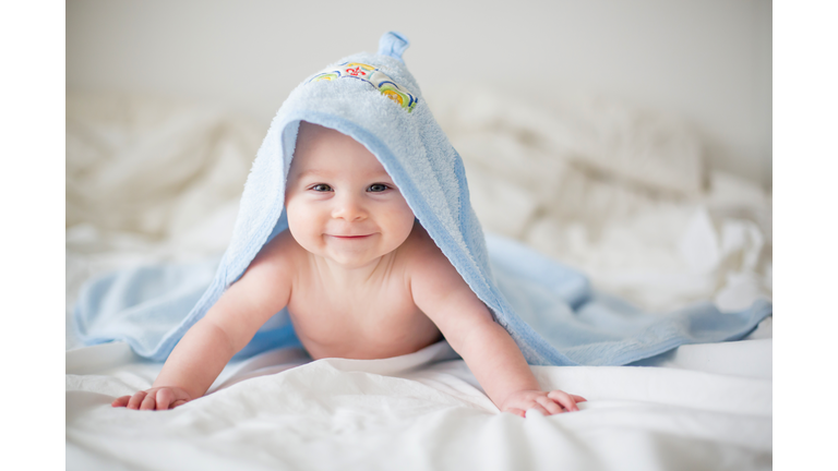 Cute little baby boy, relaxing in bed after bath, smiling happily