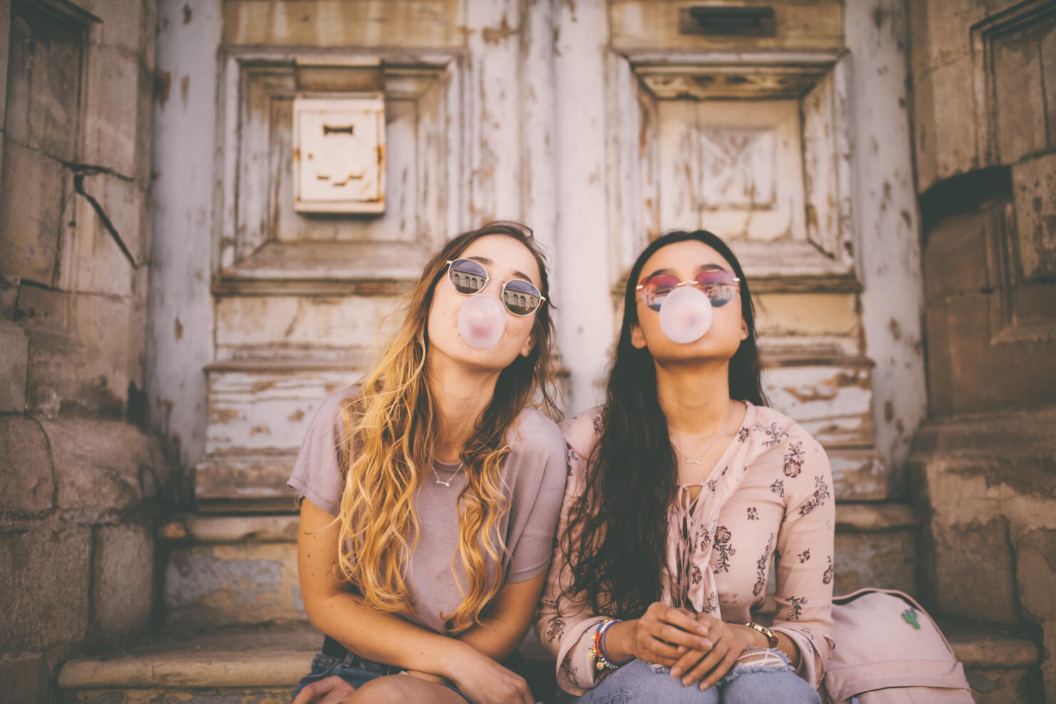 Playful young women blowing pink bubble gums in old city