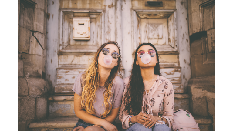 Playful young women blowing pink bubble gums in old city