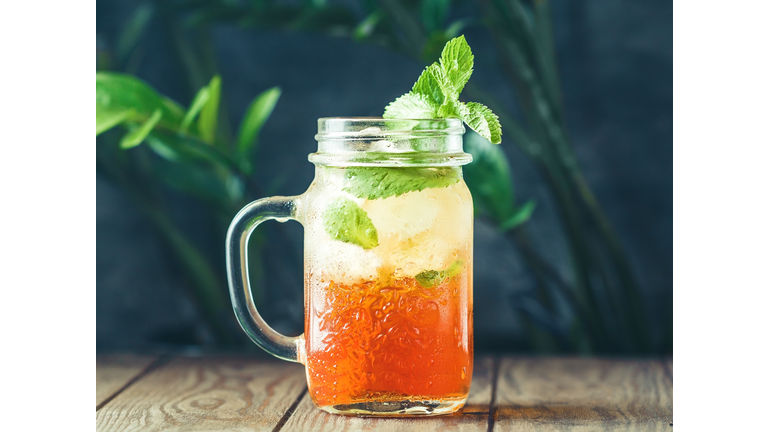 Ice black tea in a glass jar with fresh mint on a wooden table.