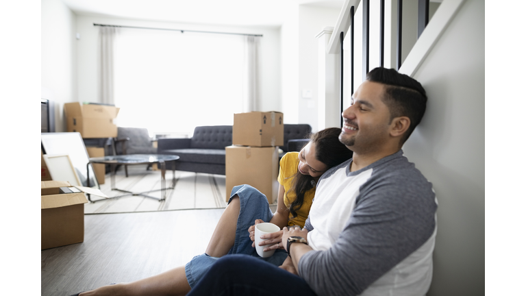 Affectionate, happy couple taking a break from moving, drinking coffee on floor