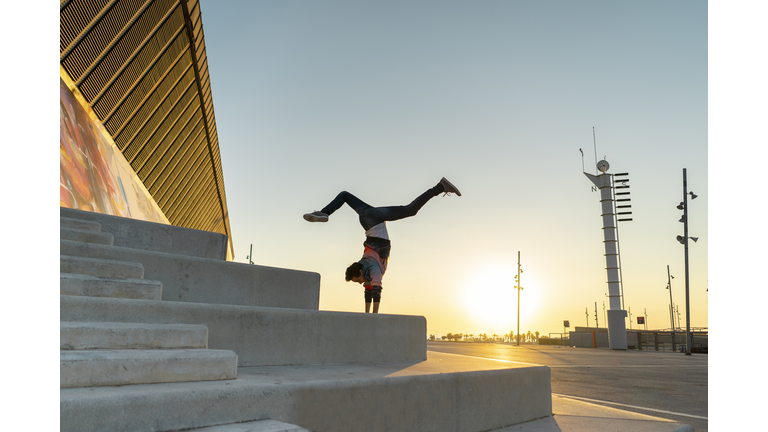 Acrobat doing handstand on stairs at sunrise