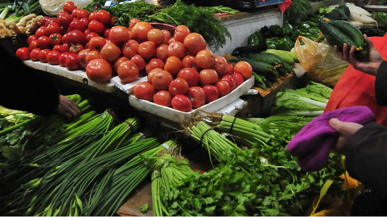 A vegetable vendor counts money as peopl