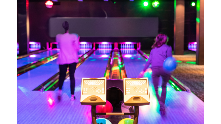 Computer monitors against teenage girls throwing balls on parquet floor at bowling alley