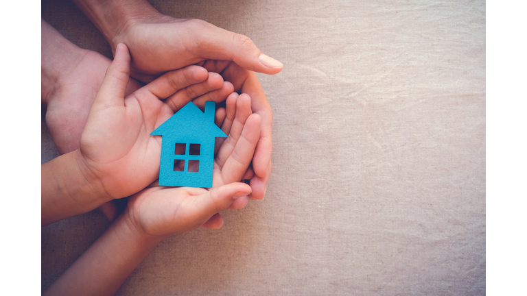 Adult and child hands holding paper house, family home and real estate concept