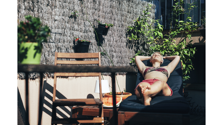 Young woman sunbathing on deck chair on her terrace