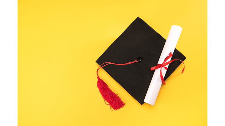 Top view of graduation mortarboard and diploma on yellow background, education concept