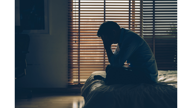 Sad businessman sitting head in hands on the bed in the dark bedroom with low light environment, dramatic concept, vintage tone color