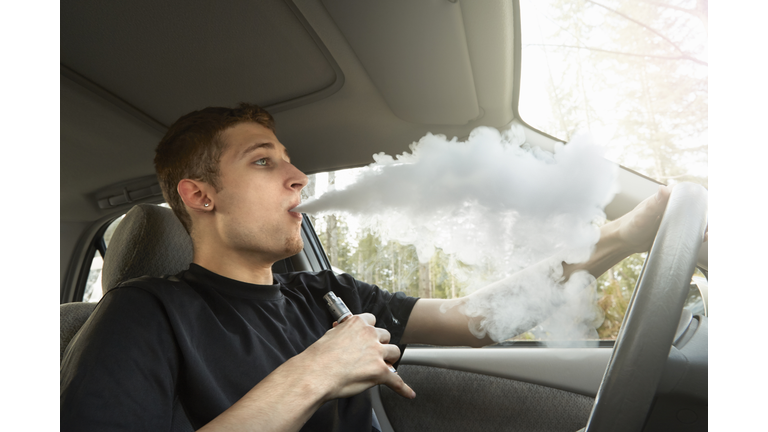 Young man driving car, smoking ecigarette