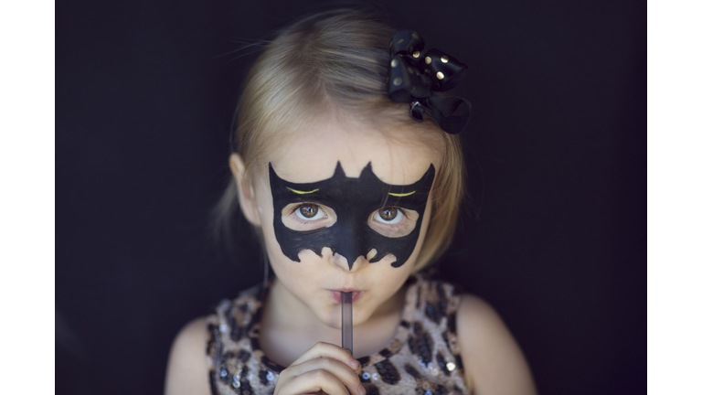 Girl with bat shaped Halloween face paints, drinking through a straw