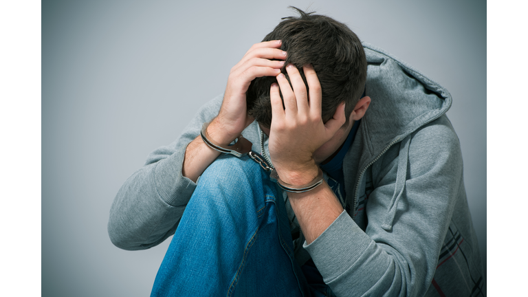 A handcuffed teenager holding his head in shame