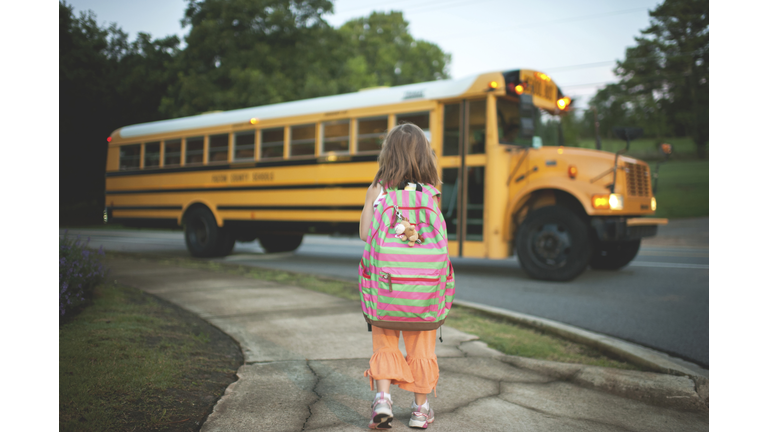 Rear view of schoolgirl with backpack waiting for bus while standing on footpath