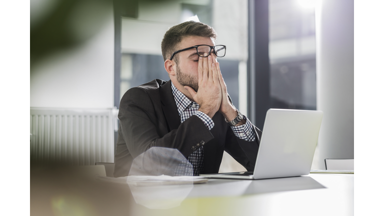 Exhausted young man with laptop in office