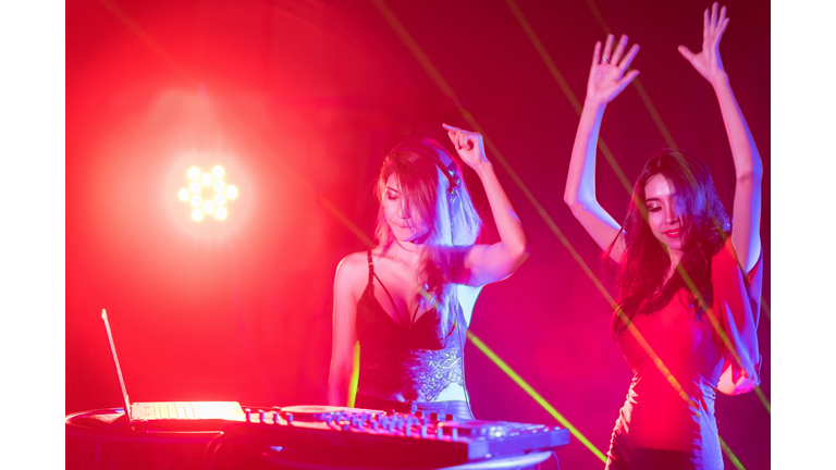 Portrait of active pretty young DJ woman playing music on laser lighting background