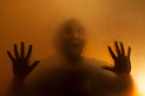 Man with hands pressed up against glass behind translucent facade