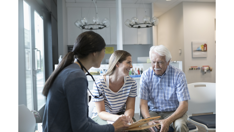 Female doctor talking with senior male patient in clinic waiting room