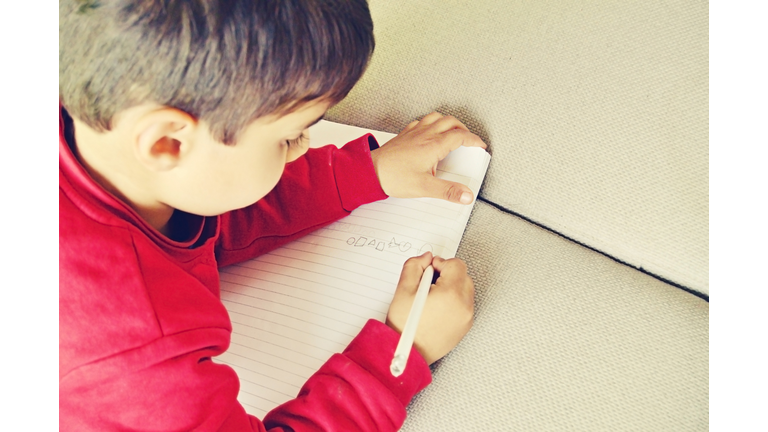 One lovely pre school kid writing on a notebook with a pencil