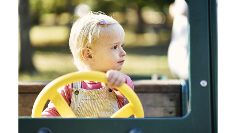 Little girl pretending to drive a car at the playground in the park