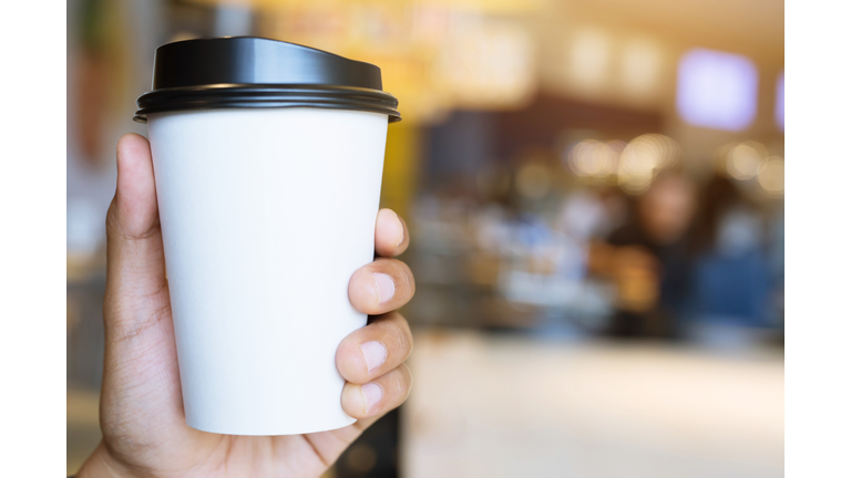 people hand holding paper cup of take away drinking coffee show on clear sky blue natural morning sunlight. space Place for your text or logo. empty space for text.