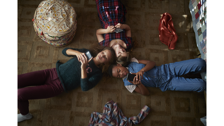 Top view of 3 tween girls looking at their smartphones