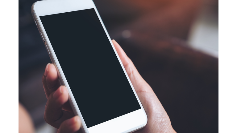 Mockup image of a hand holding white mobile phone with blank black desktop screen with blur background