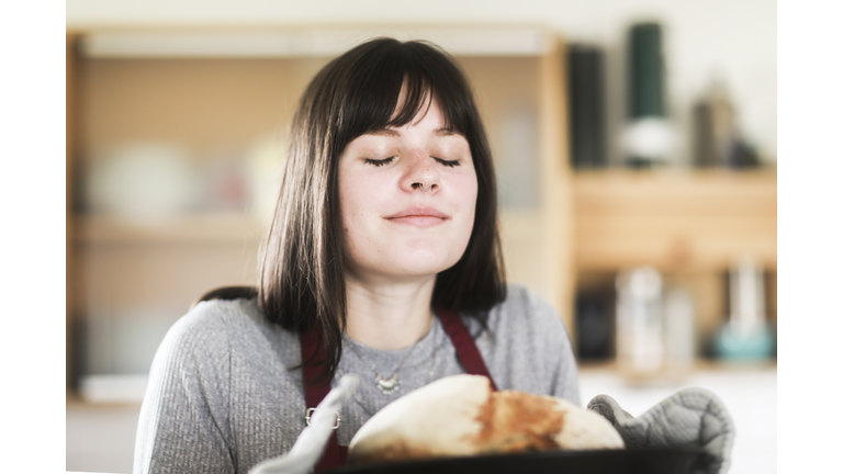Smiling Woman standing in the kitchen holding a freshly baked loaf of bread