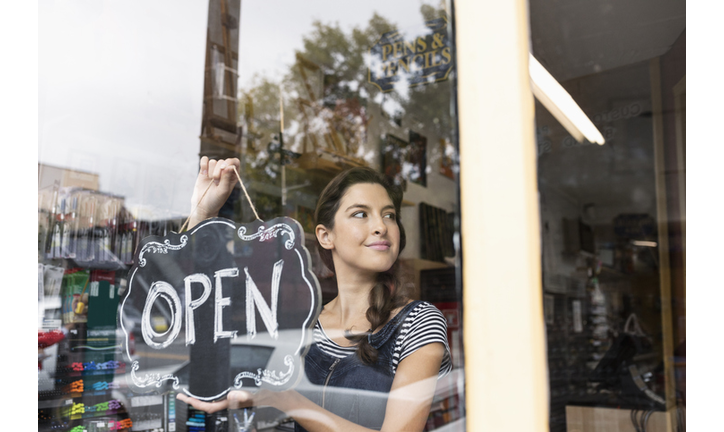 Confident female small business owner hanging Open sign in shop window