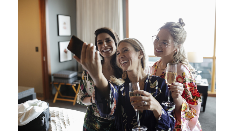 Happy women friends drinking champagne and taking selfie in hotel room, enjoying spa weekend