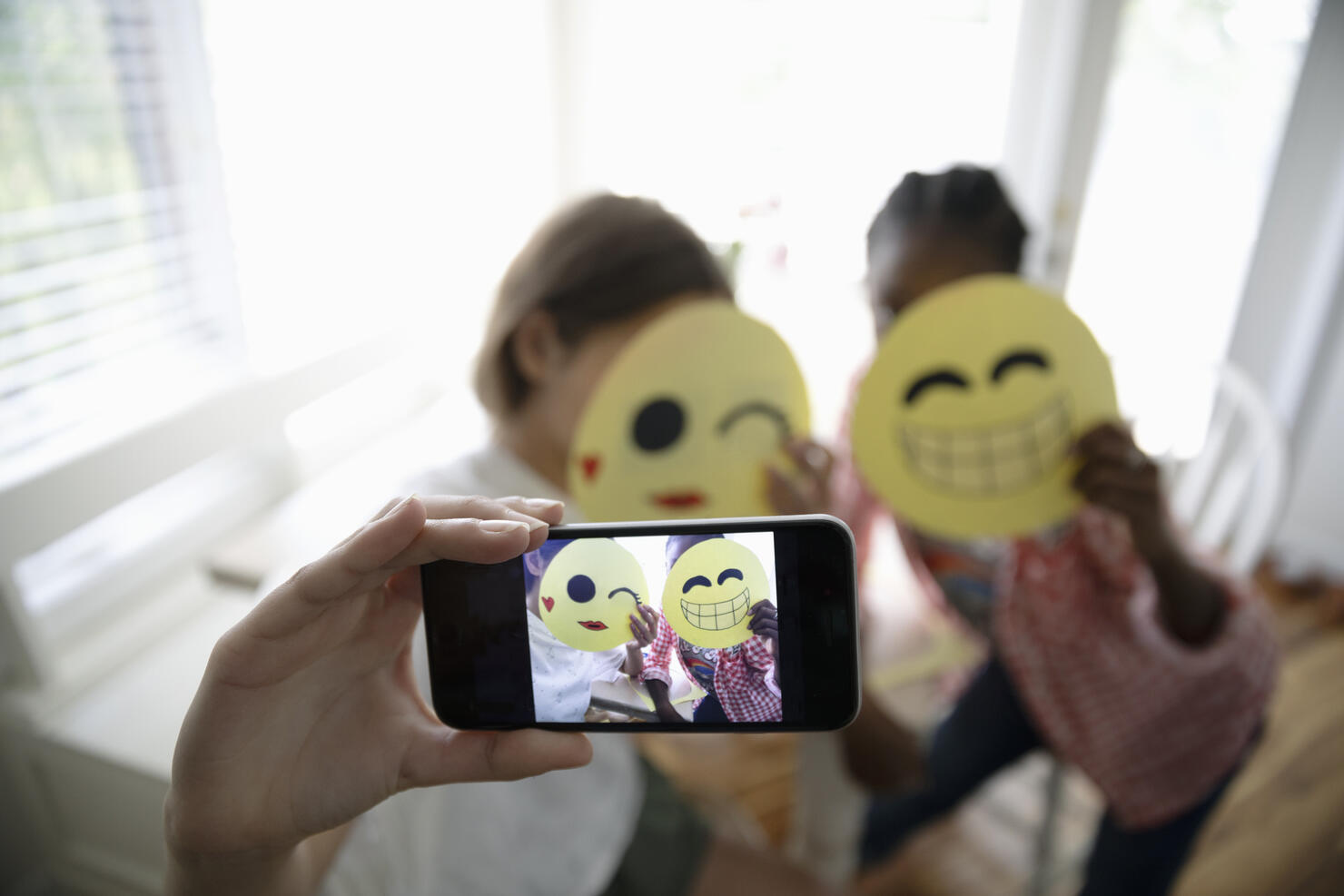 Tween girl friends with camera phone taking selfie, holding smiling emoji art projects