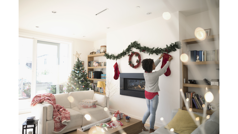 Woman hanging Christmas stocking above fireplace in living room