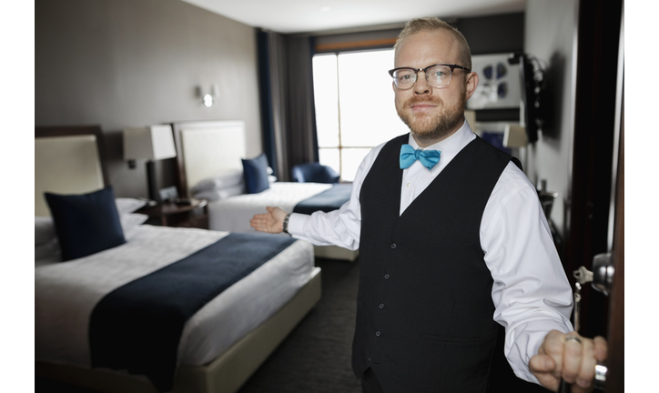 Portrait friendly male hotel bellhop opening hotel room door