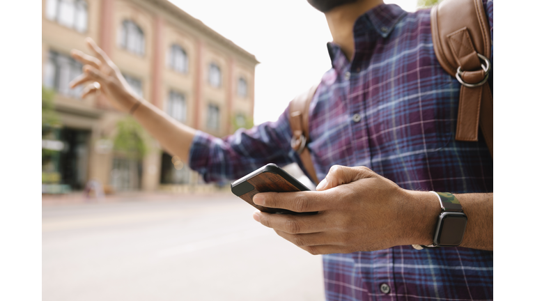 Young man with smart phone hailing a taxi on urban street