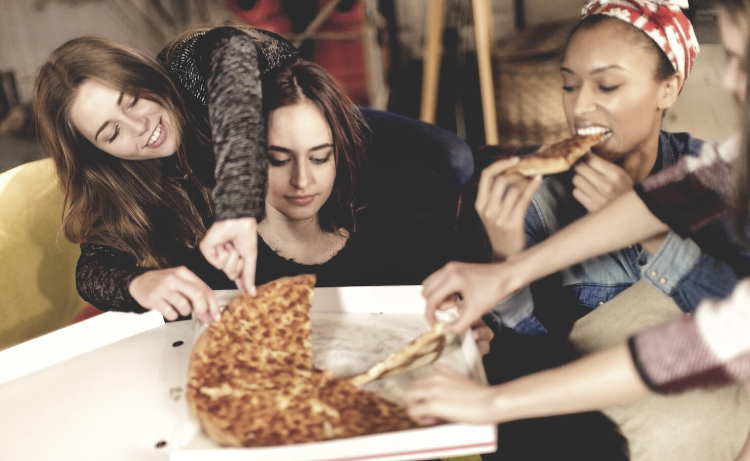 Four young women sitting round a table, eating pizza.