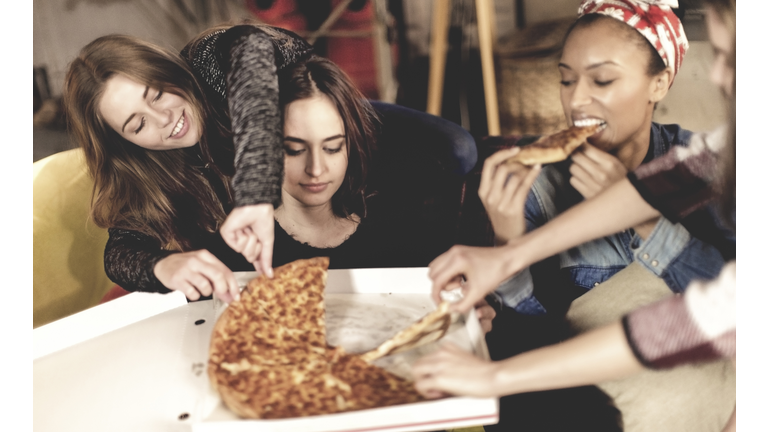 Four young women sitting round a table, eating pizza.