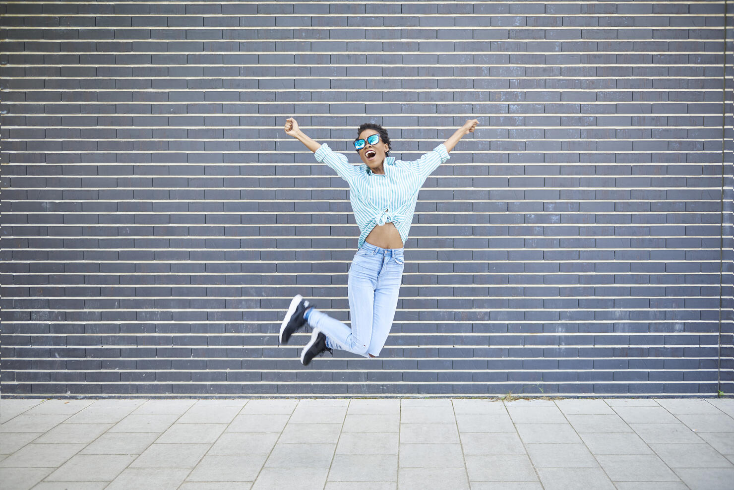 Happy woman jumping in the air in front of grey facade