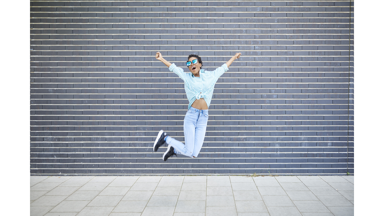 Happy woman jumping in the air in front of grey facade