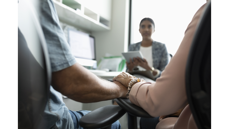 Senior couple holding hands, talking with doctor in clinic office