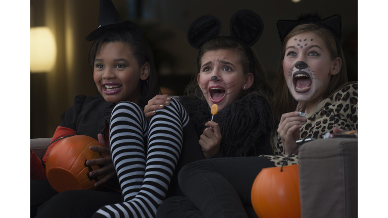 Girls in costumes watching scary movie together on Halloween