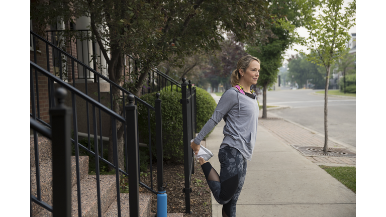 Female runner stretching legs on sidewalk