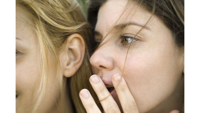 Young woman whispering secret into friend's ear, close-up