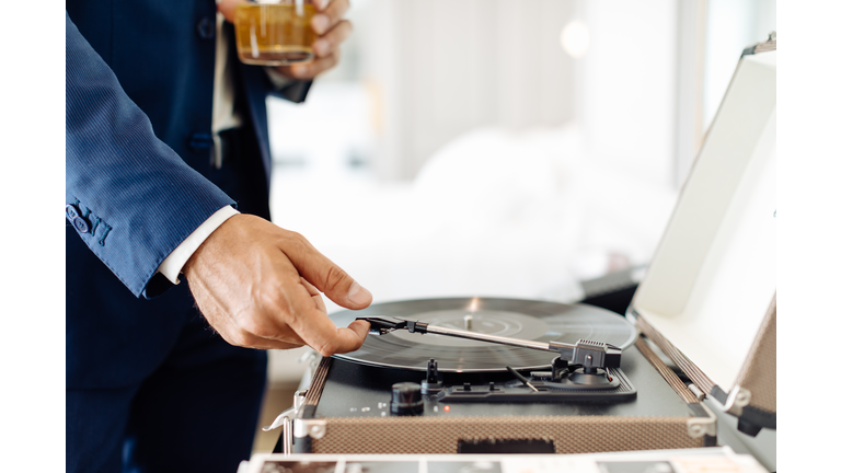 Businessman with iced drink, playing turntable in suite
