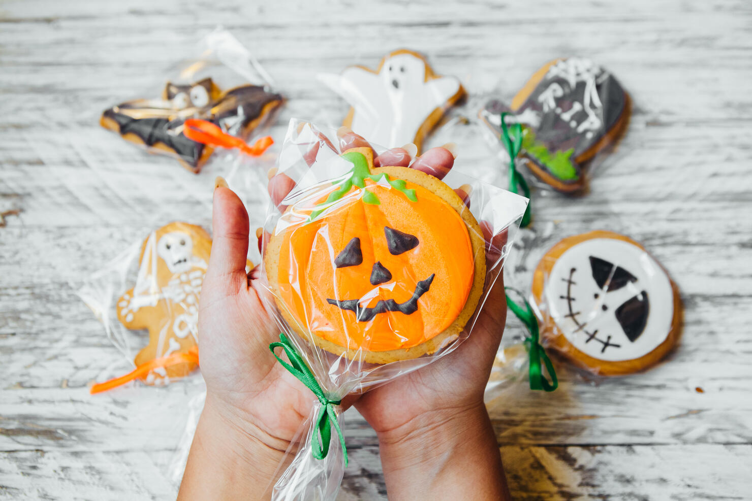 Cropped Hands Of Woman Holding Various Cookies Wrapped In Plastic Over Wooden Table During Halloween
