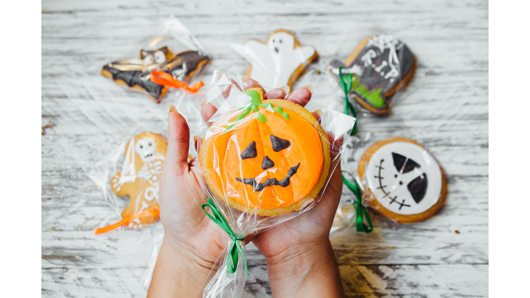 Cropped Hands Of Woman Holding Various Cookies Wrapped In Plastic Over Wooden Table During Halloween