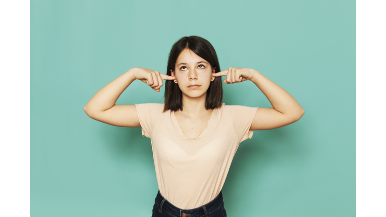 Girl looking up while covering ears against turquoise background