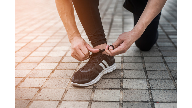 Low Section Of Man Tying Shoelace While Kneeling On Footpath