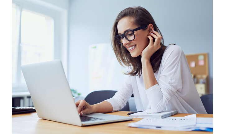 Portrait of beautiful cheerful young businesswoman working on laptop and laughing in home office