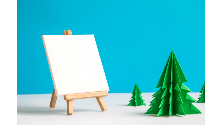 Easel and blank art canvas with origami christmas trees winter landscape abstract.