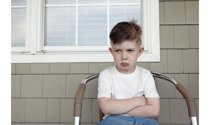 Portrait of boy sitting outside house sulking